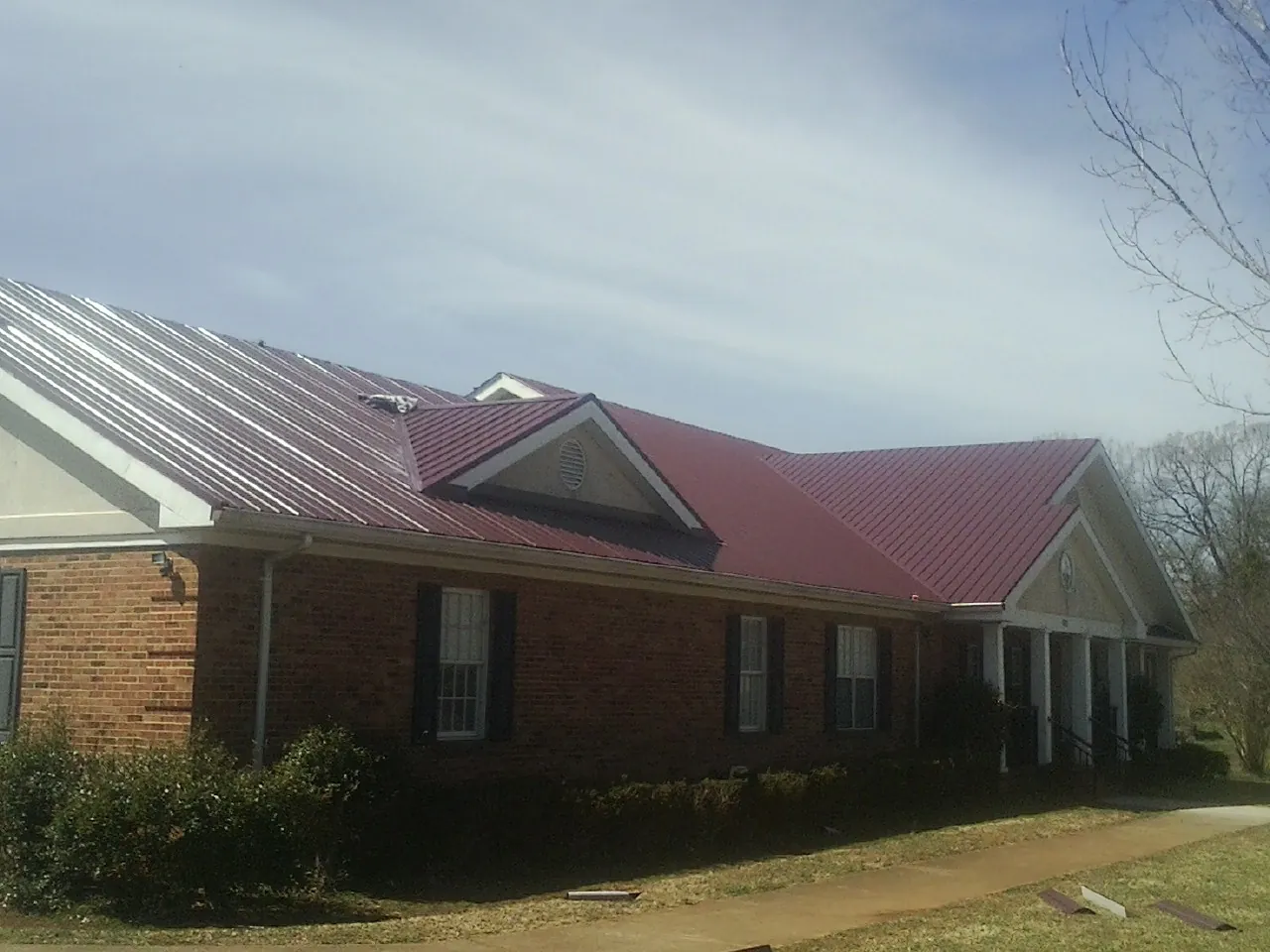 Red metal roof with gabled entries on a long brick building, from a Hail Damage Roof Repair job in Harcourt