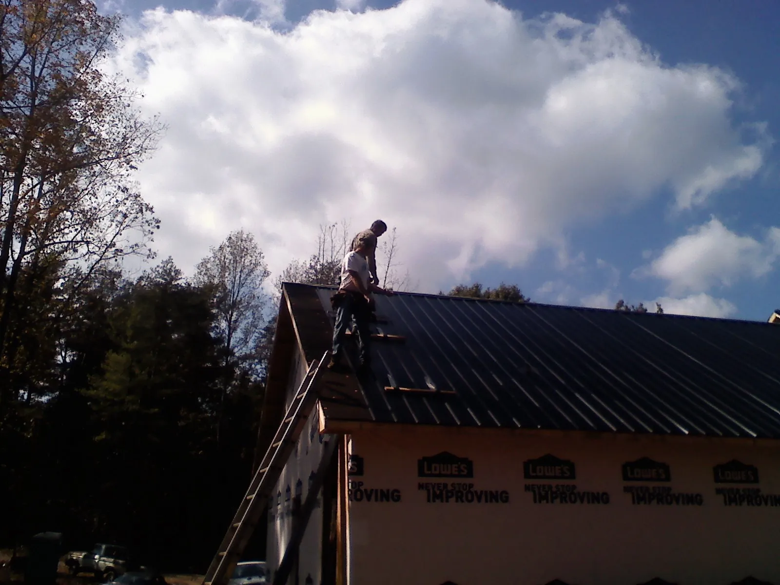 Roofer fastening dark metal panels high against a cloudy sky, from a Roof Inspection job in Harcourt