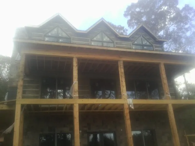 Dormers and porch framing on a large log home under construction — Roof Coating work by our crew in Harcourt