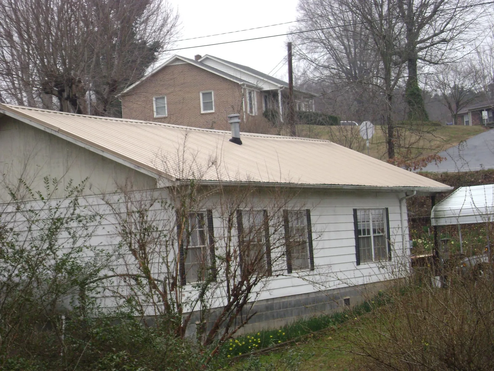 Tan metal roof on a white sided house set into a hillside — Commercial Roofing by Roofing Brothers in Harcourt