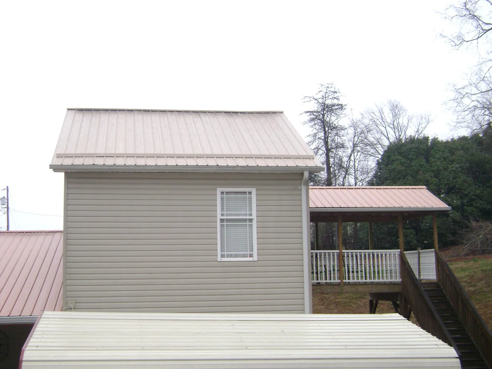 Tan metal roofs on a two story addition and attached porch, from a Roof Replacement job in Harcourt